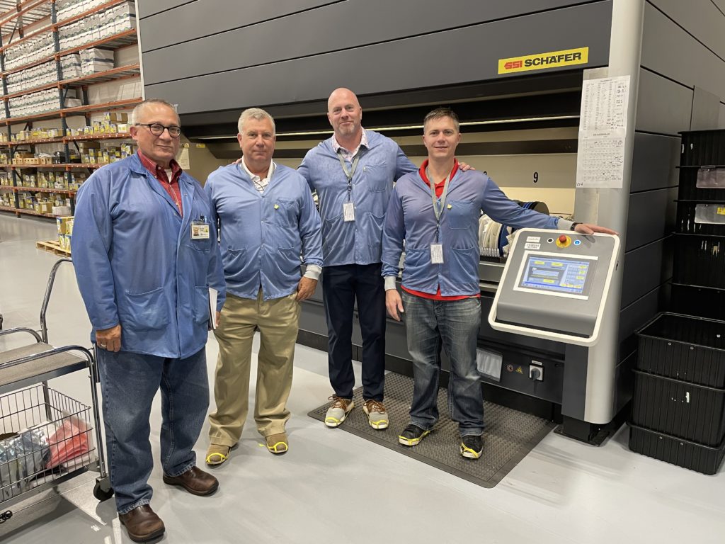 Fairchild Equipment's President Van Clarkson, Mike Bruno, and Broc Riedner standing with Keytronic's Kevin Gregg in front of vertical lift module