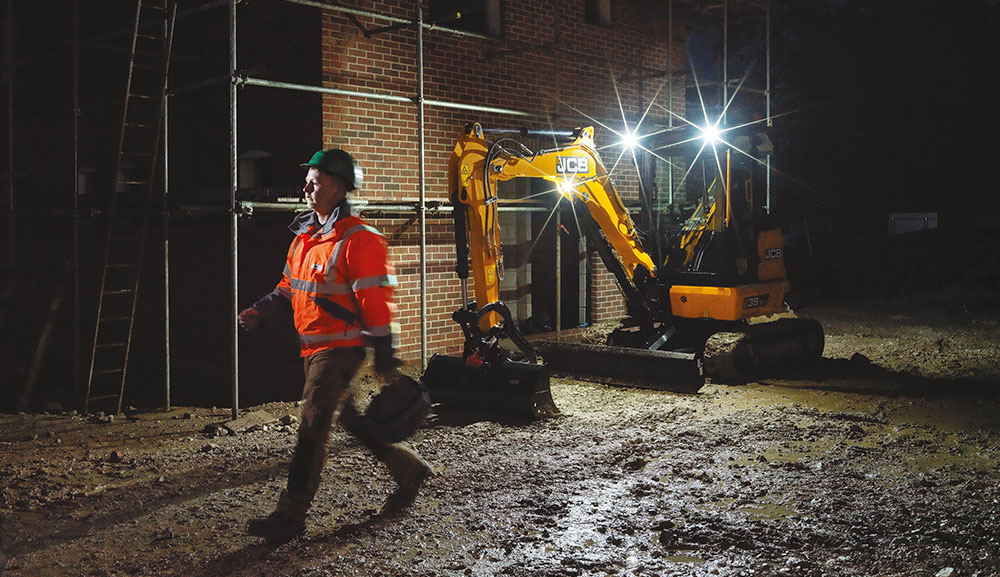JCB 35z-1 compact excavator with lights on at dark construction site.
