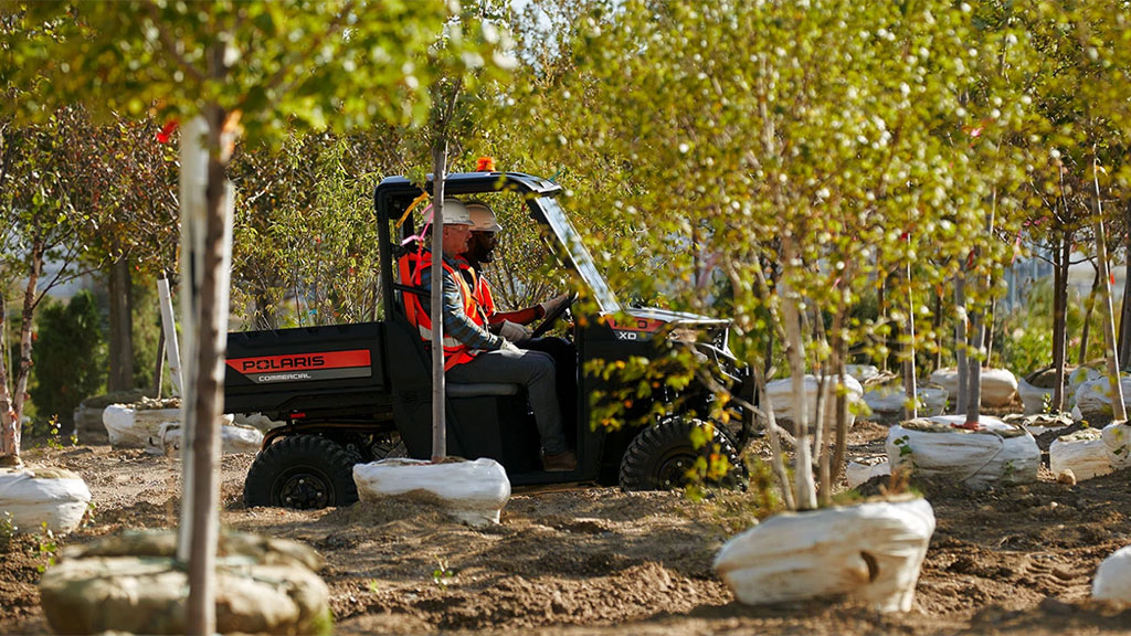 Pro XD Mid-Size Gas Utility Vehicle by Polaris Commercial driving up dirt hill on work site.
