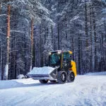 JCB 215 Skid Steer driving on snowy road with snow in bucket attachment.