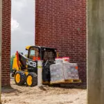 JCB 215 Skid Steer carrying pallet of materials at construction site.