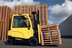 Hyster E30-40XN electric forklift transporting empty pallets outdoors, with a blue cloudy sky.