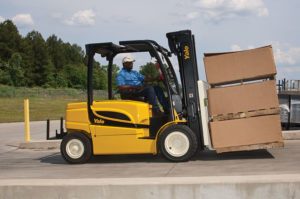 Yale ERP-VM electric lift truck transporting pallets of boxes outdoors, with green trees in the background.