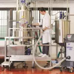 Operator using Nilfisk S2 professional vacuum hose attachment to clean up work area.