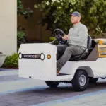 Taylor-Dunn Bigfoot S Burden Carrier driving outdoors, with materials on bed.