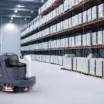 Advance SC5000 rider scrubber next to pallet racking in a warehouse.