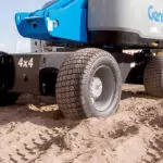 Genie S-65 HF boom lift wheels on rough dirt terrain.