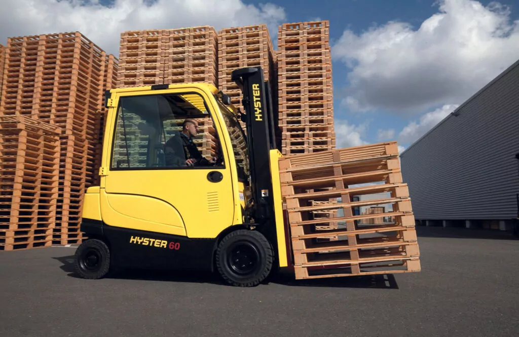 Hyster J60XN electric forklift transporting a stack of empty pallets in an outdoor lot.