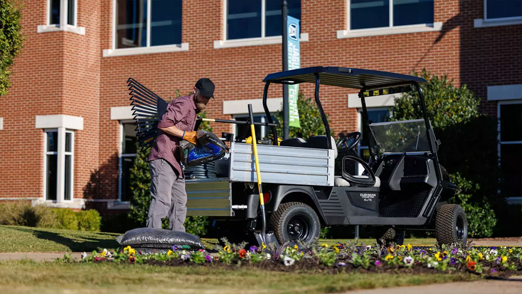 Worker getting materials out of Cushman Hauler Pro utility vehicle cargo bed.