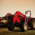 Mahindra 4540 4WD Tractor driving in a field with logs in bucket loader attachment.