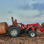 Mahindra 4540 4WD Tractor with special attachments transporting 2 bales of hay through crop field.