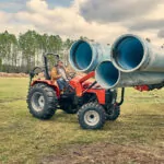 Mahindra 4540 4WD Tractor transporting large pipes through grass field.