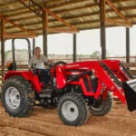 Mahindra 5155 4WD Tractor with rake attachment driving through sandy enclosure.