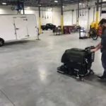 Employee cleaning garage floor with walk-behind Kodiak K16 disk floor scrubber.