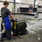 Kodiak K16 walk-behind scrubber with disk deck cleaning messy floors in manufacturing facility.