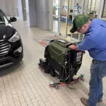 Employee cleaning automotive showroom floors with Kodiak K19 walk-behind cylindrical scrubber.