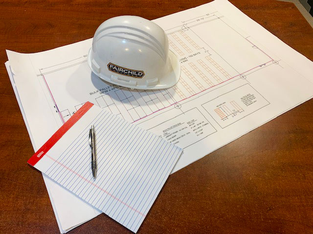 Warehouse layout blueprints, note pad, and hard hat.