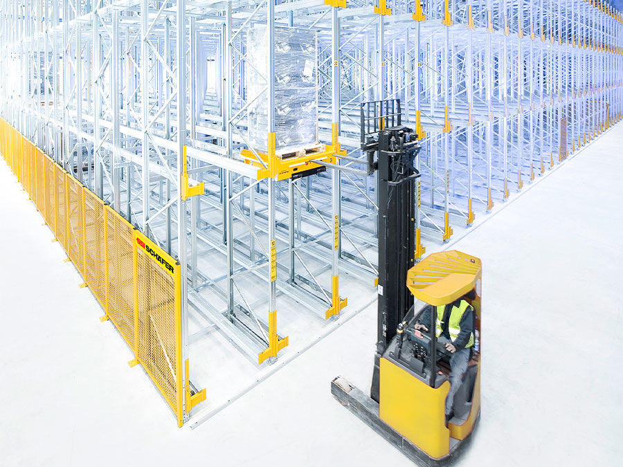 Narrow aisle forklift lifting pallet onto racking SSI Schaefer pallet shuttle in warehouse.