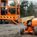 JLG 670SJ self-leveling boom lift driving on dirt at jobsite.