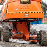 JLG 670SJ telescopic self-leveling boom lift driving in dirt.
