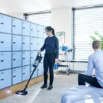 Worker cleaning floors with Advance VU200 upright vacuum in storage room.