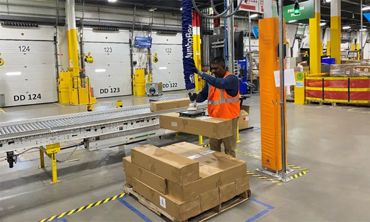 worker using vacuum lifter to lift box off pallet in warehouse.