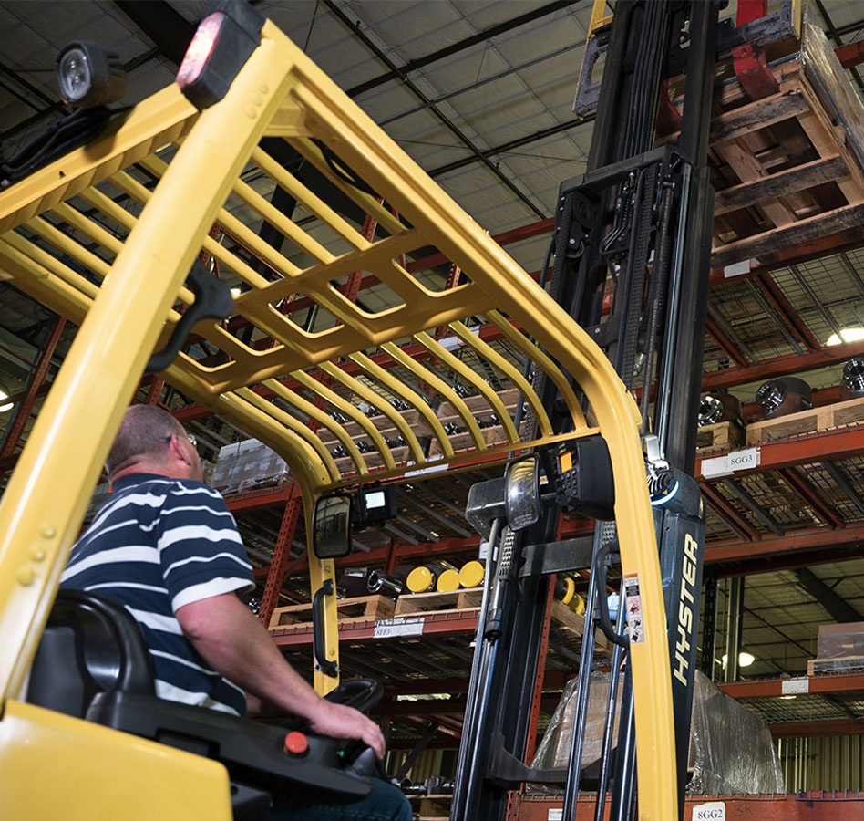 Worker lifting pallet off warehouse racking with Hyster forklift.