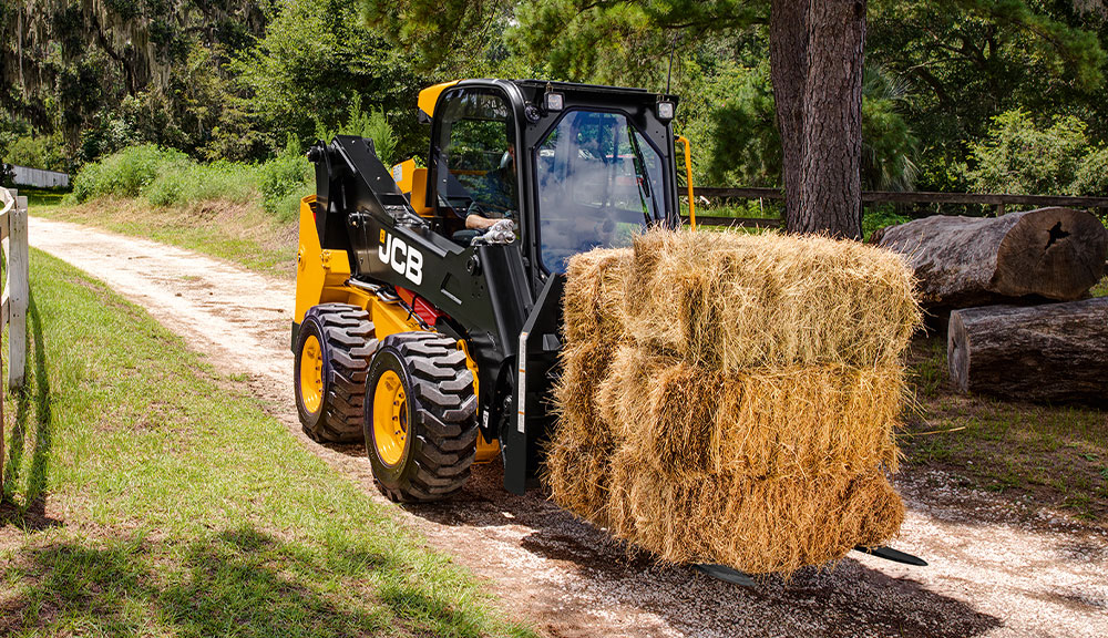 JCB 215 skid steer loader transporting hay bale.
