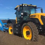JCB 4220 Fastrac Icon agricultural tractor driving through large dirt rivets on farm.