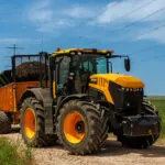 JCB 8330 Fastrac agricultural tractor driving on dirt road near farm fields.